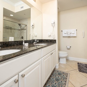 The master bathroom features a stylish double vanity with dark granite countertops, an an elegant glass tile shower