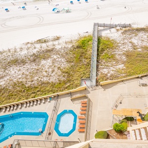 Aerial balcony view showcasing the pool area with lounge chairs, leading to a path that connects to the beach and white sand