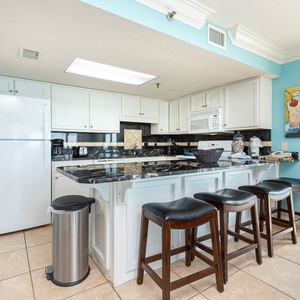 Bright kitchen featuring white cabinetry, dark granite countertops, and bar seating, complemented by colorful art