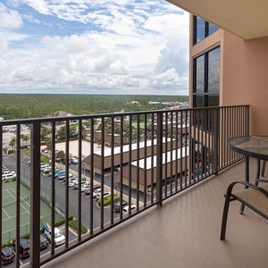 Enjoy a relaxing moment on the master balcony with a glass table, overlooking lush greenery and nearby tennis courts