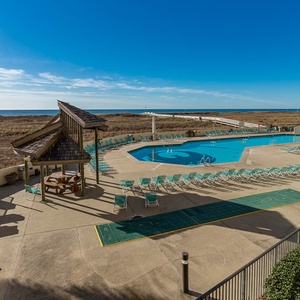 Expansive pool area with lounge chairs and a view of the beach, framed by palm trees and a clear blue sky