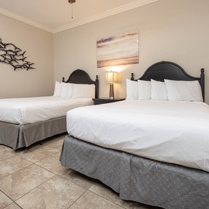 This guest bedroom features two cozy queen beds, stylish decor, and a serene beach-themed artwork for a relaxing stay
