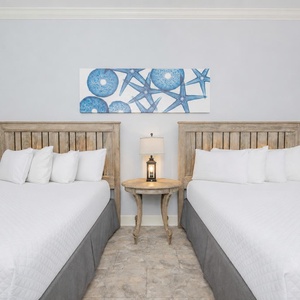 Relaxing guest bedroom featuring two cozy queen beds, beach-themed decor, and a charming nightstand with a lamp