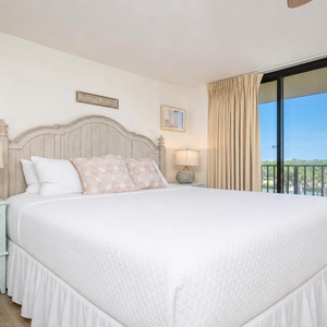 Bright and airy master bedroom featuring a king bed, decorative pillows, and a balcony with a scenic view