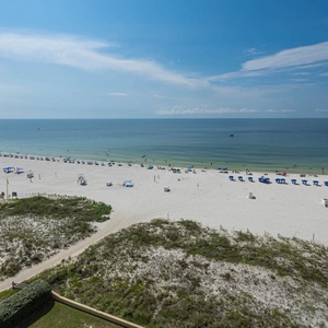 Expansive view of the beach with white sand, colorful umbrellas, and sun loungers lining the shore under a clear blue sky