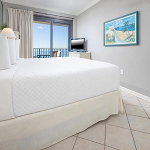 Bright and airy master bedroom featuring a king bed, a TV, and a balcony with views of the beach, perfect for relaxation