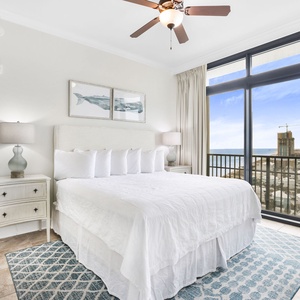 This bedroom features a plush white king bed, soft blue accents, and large windows offering a stunning beach view