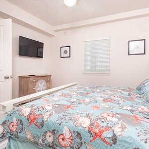 This cozy bedroom features a vibrant starfish-patterned quilt, a mounted TV, and soft natural light from the window