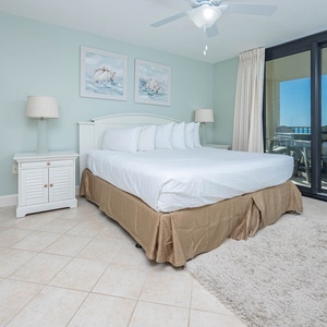 Master bedroom featuring a king bed, soft rug, and sliding glass doors leading to a balcony with beach views
