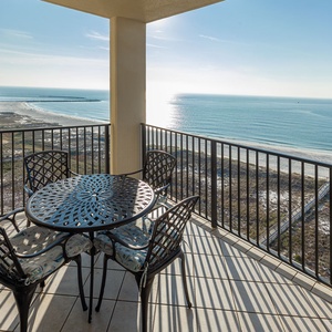 Balcony with a round table and chairs offers a serene view of the tranquil beach and sparkling gulf waters