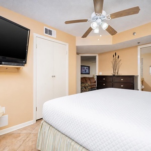 Bright bedroom featuring a king bed, TV, and a tasteful dresser, with the en-suite bathroom visible in the background
