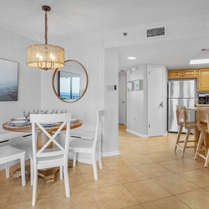 The dining area features a round wooden table with white chairs, complemented by a stylish light fixture and wall art