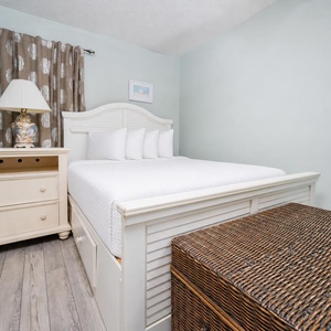 This cozy bedroom features a white bed with plush pillows, a stylish lamp, and a charming wicker storage chest