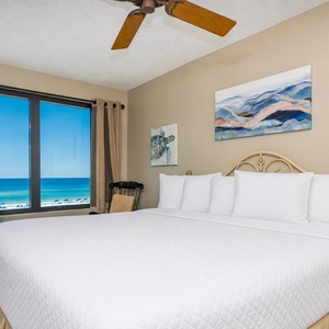This bedroom features a king-sized bed, a TV, and stunning beachfront views through large windows