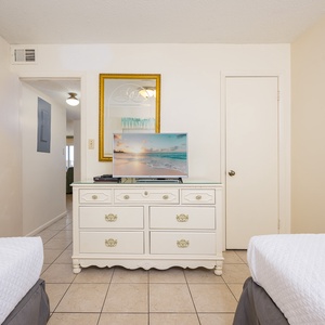 This guest bedroom features two beds, a TV on a stylish white dresser, and a welcoming view into the hallway
