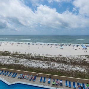 The view showcases a vibrant beach scene with colorful umbrellas, sun loungers, and a sparkling pool area below