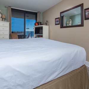 Inviting master bedroom features a plush king bed with crisp linens, a TV, and access to a balcony with views of the gulf