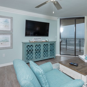 Bright aqua accents complement the cozy living area, featuring a queen sofa-sleeper, large TV, and a view to the beach