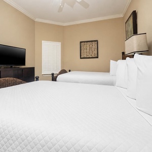 This cozy guest bedroom features two comfortable queen beds, a TV for entertainment, and warm, inviting decor