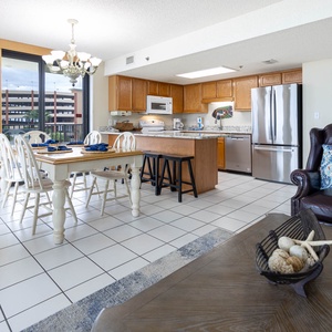 Bright dining area features a wooden table set for five, with a cozy leather chair and a modern kitchen in the background