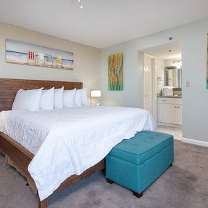 The master bedroom features a plush king bed, vibrant artwork, and a stylish turquoise ottoman, creating a relaxing retreat