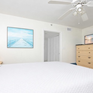 Bright guest bedroom featuring a queen bed, light-colored furniture, a TV, and coastal artwork that enhances the serene vibe