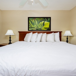 This inviting bedroom features a plush king bed with crisp white linens, complemented by tropical artwork and soft lighting