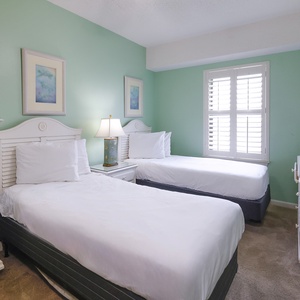 This guest bedroom features two twin beds, a light green accent wall, and a stylish dresser with a flat-screen TV