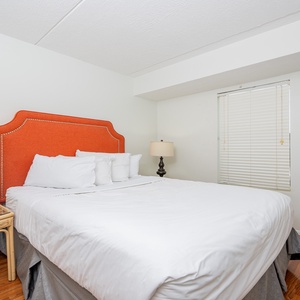 This inviting bedroom features a bright orange headboard, cozy bedding, and a charming bedside lamp for a restful stay