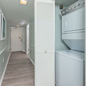 A laundry area features a stacked washer and dryer, complemented by soft blue walls and framed nautical artwork