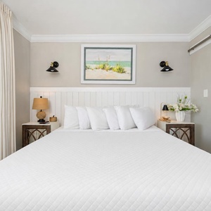 Elegant master bedroom featuring a plush king bed, stylish lamps, and beach-themed artwork for a relaxing getaway