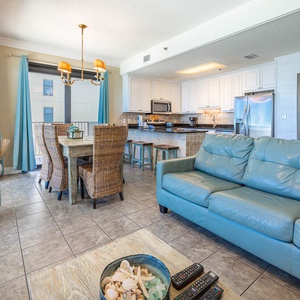 Bright living space featuring a turquoise sofa, dining area with woven chairs, and a modern breakfast bar for entertaining