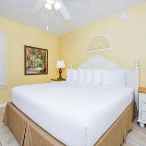Bright yellow walls complement the cozy king bed, while a decorative painting and lamps add warmth to this inviting bedroom