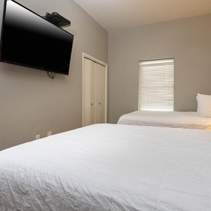 Guest room featuring two queen beds, a wall-mounted TV, and natural light from the window, creating a welcoming atmosphere