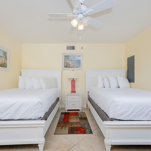 Relax in the guest bedroom featuring two double beds, a cozy lamp, and cheerful coastal artwork