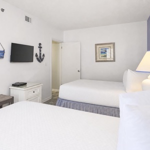 Cozy guest bedroom featuring two double beds, a wall-mounted TV, and nautical decor for a relaxing beach getaway