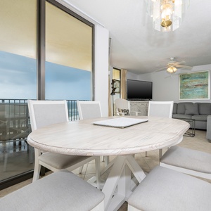 A round dining table with light gray chairs offers a cozy spot to enjoy meals, complemented by a view of the beach front