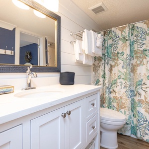 Sleek bathroom featuring a white vanity, decorative mirror, and a colorful coral-patterned shower curtain