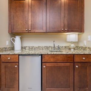 Prepare drinks at the stylish wet bar featuring rich wood cabinetry and stainless ice maker