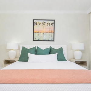 Relax in this master bedroom featuring a king bed with colorful pillows and a beautiful palm tree painting above