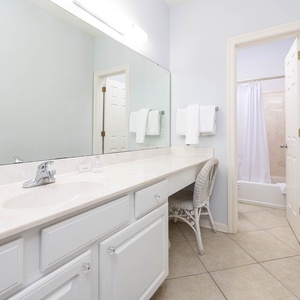 Master bath featuring a spacious vanity with a marble countertop, a wicker chair, and a tub/shower combo behind a curtain