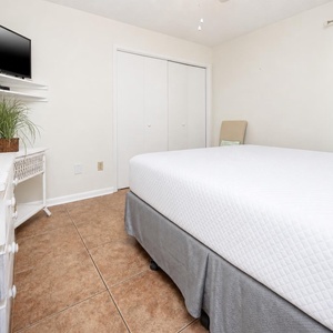 Bright and airy guest bedroom featuring a cozy queen bed, wall-mounted TV, and natural light from the window