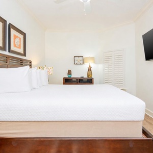 This bedroom features a large king bed with crisp white linens, a mounted TV, and charming coastal decor for a relaxing stay