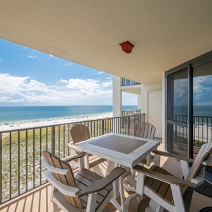 Balcony with a table and chairs offers a serene view of the white sand beach and tranquil gulf waters under a bright sky