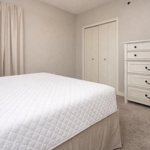 Guest bedroom featuring a queen bed, soft beige curtains, and a stylish dresser against a neutral wall