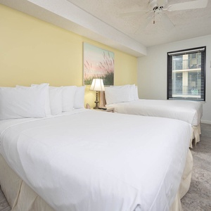 Brightly decorated rguest bedroom featuring two double beds, a bedside lamp, and a TV, providing a comfortable retreat