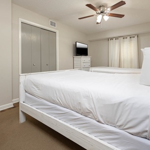 This guest bedroom features two queen beds, a ceiling fan, a TV, and light curtains that enhance a serene atmosphere