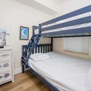 This guest bedroom features a stylish bunk bed, playful giraffe artwork, and a charming fish-themed dresser, perfect for kids