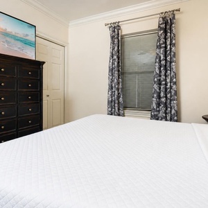 Unwind in this guest bedroom featuring a plush queen bed, decorative pillows, and a stylish dresser with a TV above