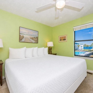 The master bedroom features a large bed, vibrant green walls, and a lovely view of the pool area and palm trees outside